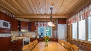 A wooden-paneled kitchen with a dining table, chairs, a stove, a refrigerator, and a window with curtains. - Tainan tupa by Interhome (Sysmä)