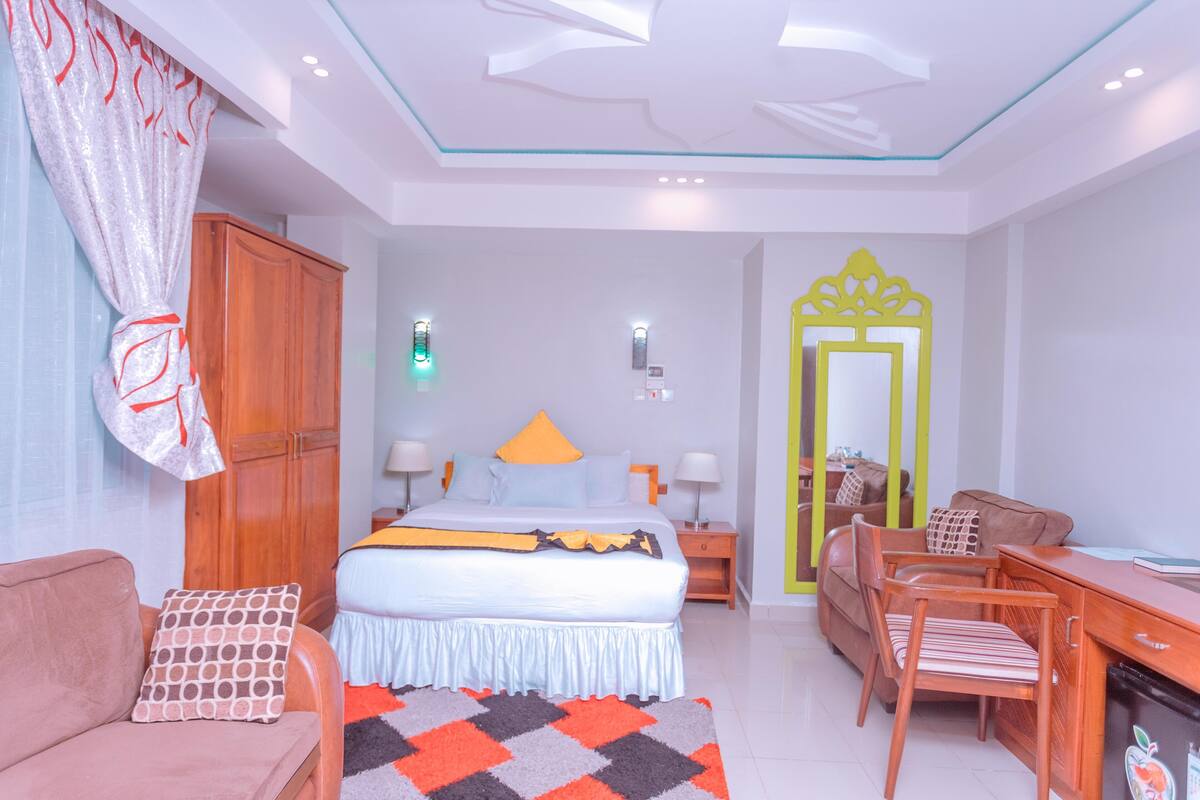A hotel room with a bed, a desk, a chair, a wardrobe, and a mirror.