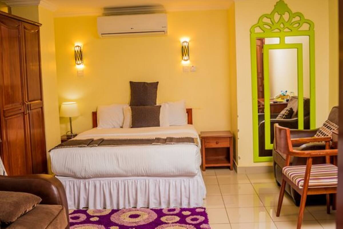A hotel room with a bed, bedside tables, a chair, a mirror, and a wardrobe.