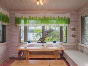 Uma mesa de jantar de madeira com bancos, uma decoração de peixe e vista para um lago através de grandes janelas.