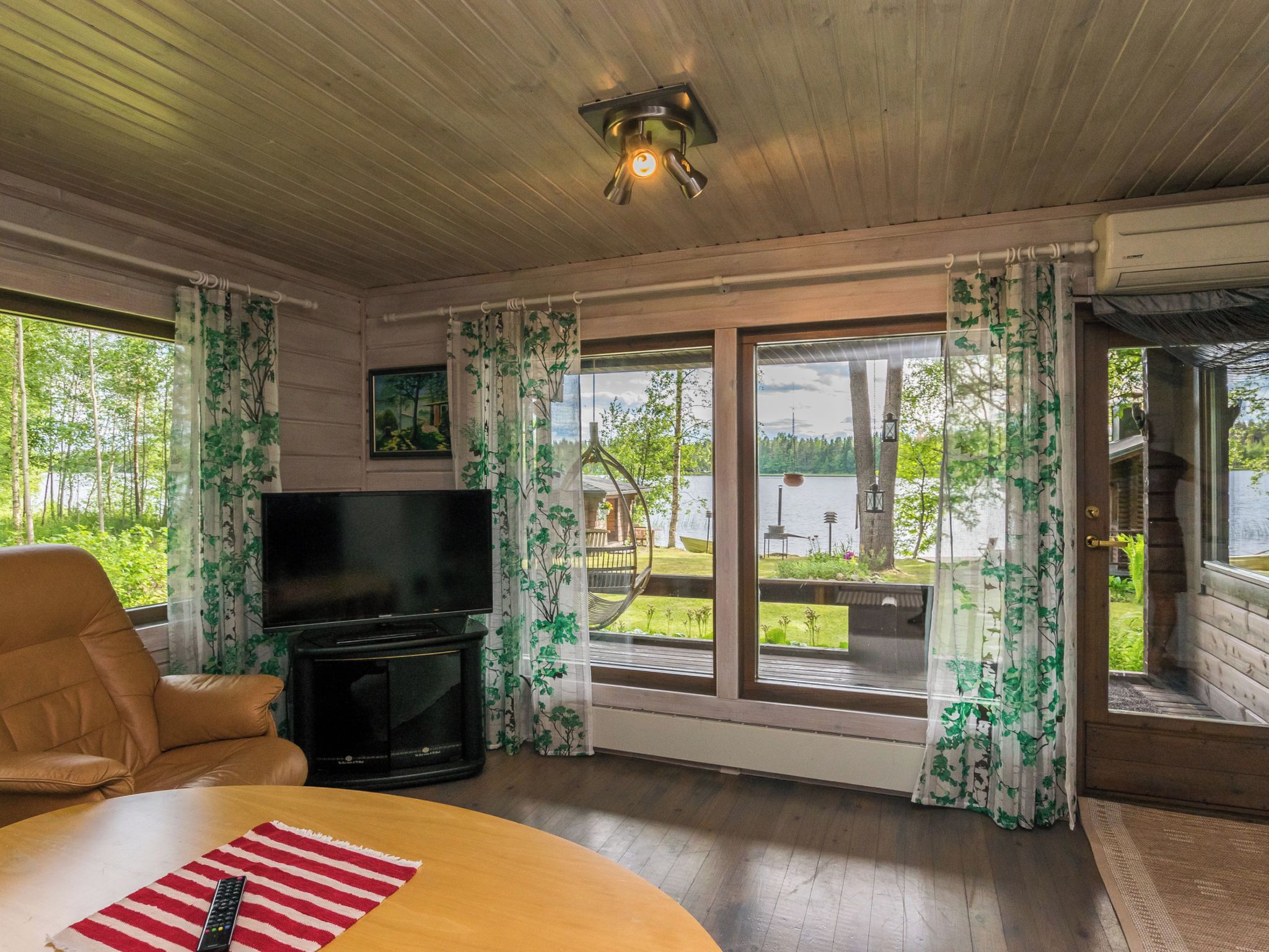 Een gezellige woonkamer met een flatscreen televisie, een comfortabele bank en een houten plafond.