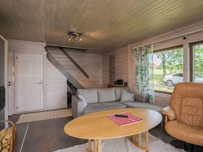 A living room with a wooden ceiling, a sofa, a coffee table, a leather armchair, and a window with curtains. - Uimaranta by Interhome (Pieksämäki)