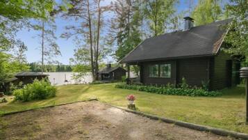 Situated in a lush environment, this cabin offers a serene escape surrounded by trees and a small lawn leading to a body of water.