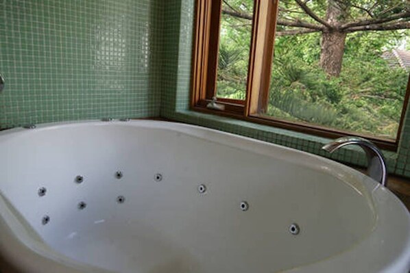 Une salle de bain avec une grande baignoire, une fenêtre donnant sur la verdure et des murs recouverts de carreaux verts.