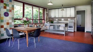 A modern kitchen with white cabinets, a granite countertop, and a built-in oven. There is a dining area with a wooden table and black chairs. - Stylish, Central, 3-Bedroom, 2-Bath Apartment in St Kilda with pool & trampoline (St Kilda)