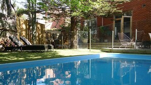 A swimming pool with a clear blue water surface, surrounded by a wooden fence and a brick building. - Stylish, Central, 3-Bedroom, 2-Bath Apartment in St Kilda with pool & trampoline (St Kilda)