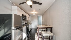 A compact kitchen with a refrigerator, microwave, and stove. There is a ceiling fan and a small table with a bench.