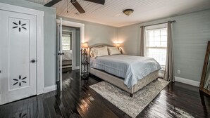 A bedroom with a bed, a ceiling fan, a nightstand, and a window with curtains.