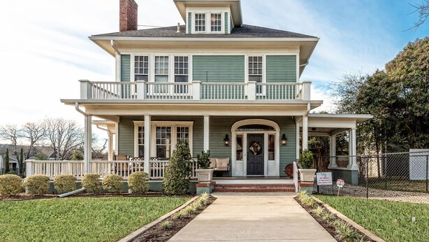 A two-story house with a front porch, a chimney, and a fenced yard.