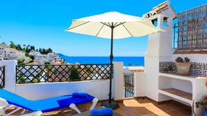 A terrace with a white umbrella, blue lounge chairs, and a view of the sea and white buildings. - Vacation home Amanda by Interhome (Nerja)