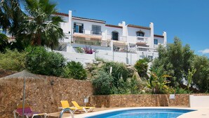 A swimming pool with lounge chairs, a stone wall, and a building with balconies in the background. - Vacation home Amanda by Interhome (Nerja)