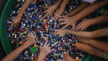 A group of people reaching into a large green bin filled with various colored building blocks.