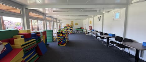 A classroom with colorful play structures, tables, and chairs arranged for learning activities.