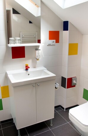 A bathroom with a white sink, a mirror, a small toy, and colorful tiles on the walls. - Museum of Bricks (Kutna Hora)