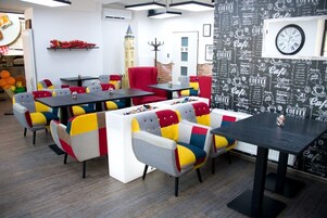 Um café moderno com cadeiras e mesas coloridas, um relógio na parede e um quadro de menu com desenhos relacionados a café.