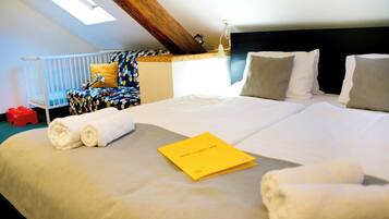 Une chambre d’hôtel avec un grand lit, une lucarne, un berceau et un petit livret jaune posé sur le lit.