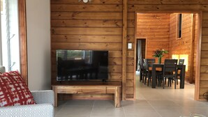 Un salón con paneles de madera, un televisor de pantalla plana, un sofá, una mesa de centro y una zona de comedor con sillas y una mesa.