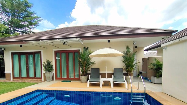 Una piscina con gradini d'accesso, circondata da un portico coperto con due poltrone da relax e un tavolo.