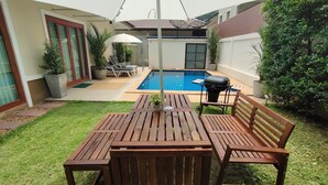 Un cortile con un tavolo e sedie di legno, un barbecue e una piscina.