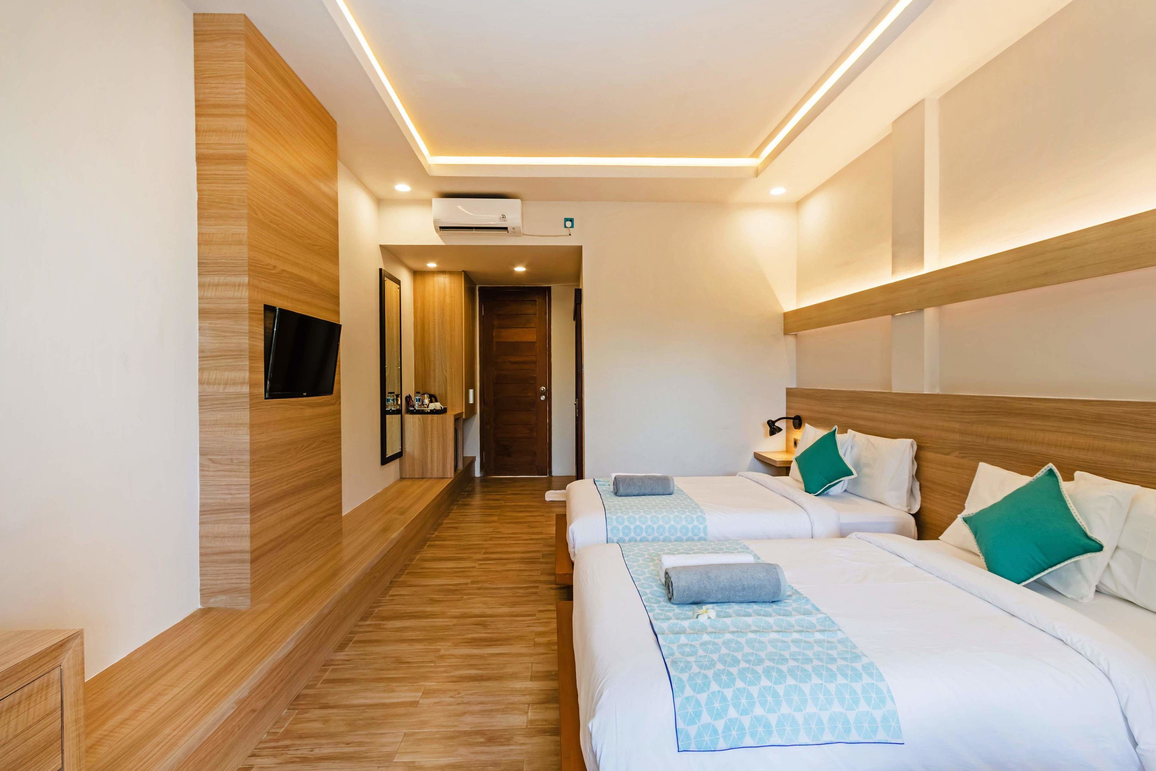 A hotel room with two beds, wooden flooring, a flat-screen TV, and a wooden headboard.