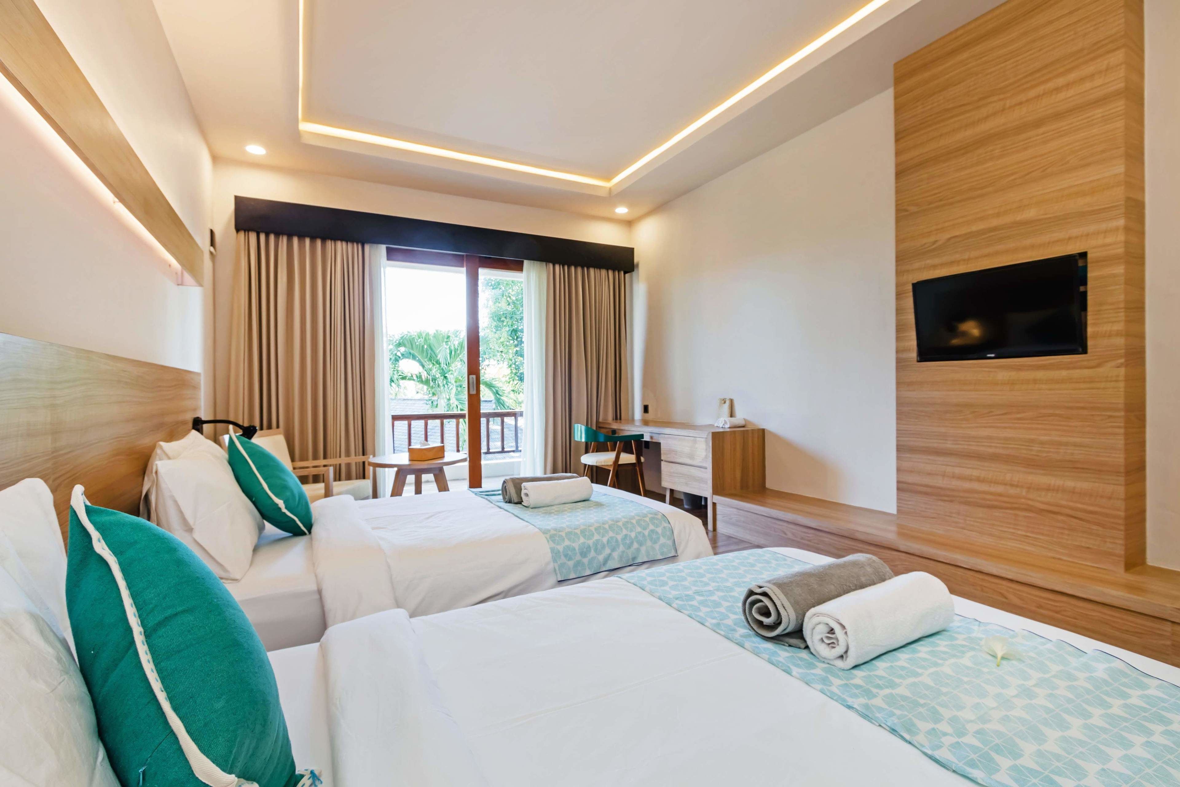 A hotel room with two beds, a desk, a chair, a TV, and a balcony with curtains.