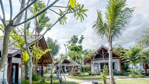 A resort with multiple wooden cabins, a central gazebo, and a well-maintained garden with palm trees and other tropical plants.