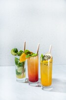 Tre bicchieri di bevande colorate con cannucce e guarnizioni.