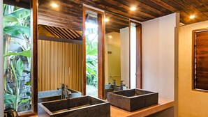A bathroom with two rectangular stone sinks, a large mirror, and a view of greenery outside.