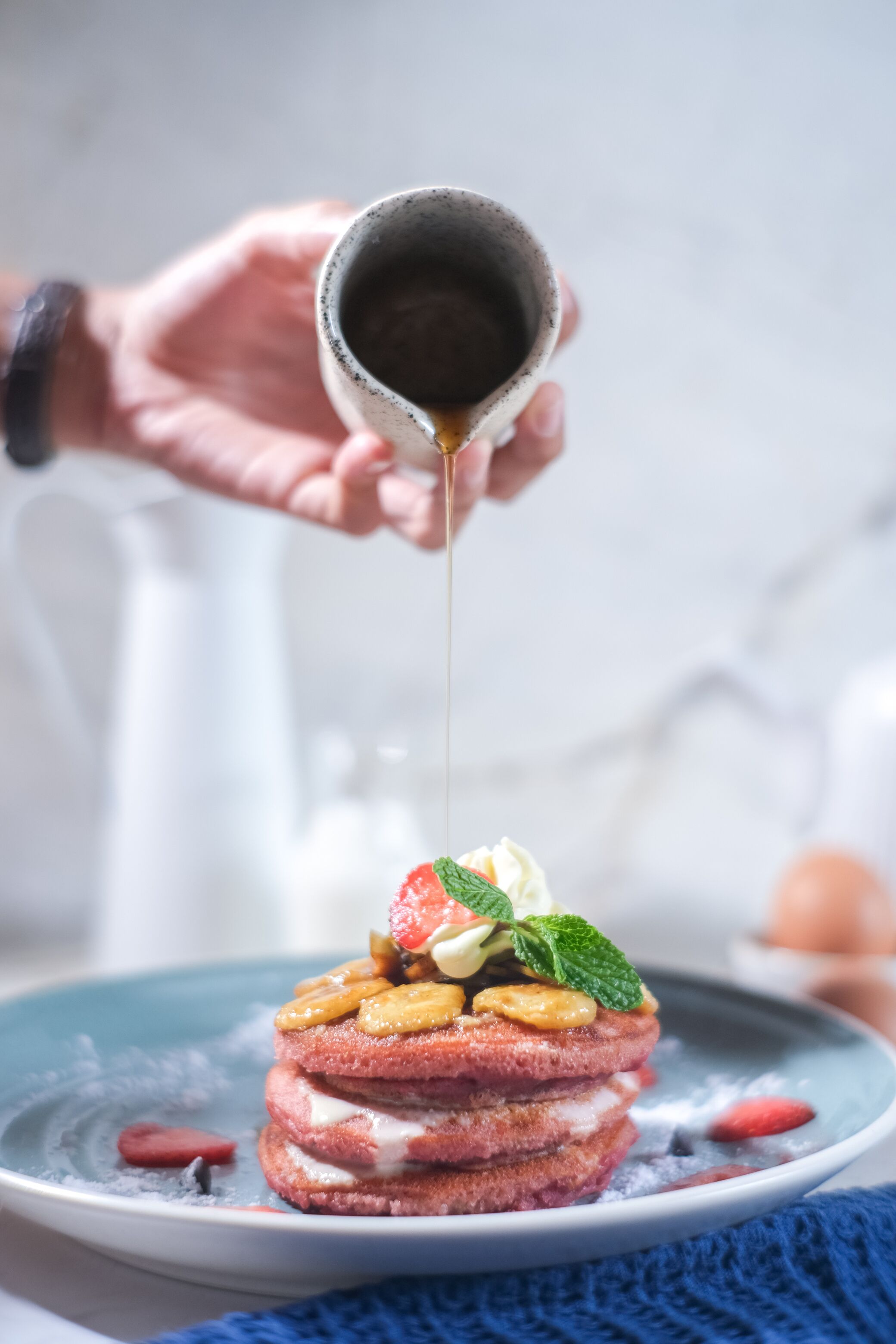 Une pile de crêpes garnie de fruits et de crème fouettée, arrosée de sirop.