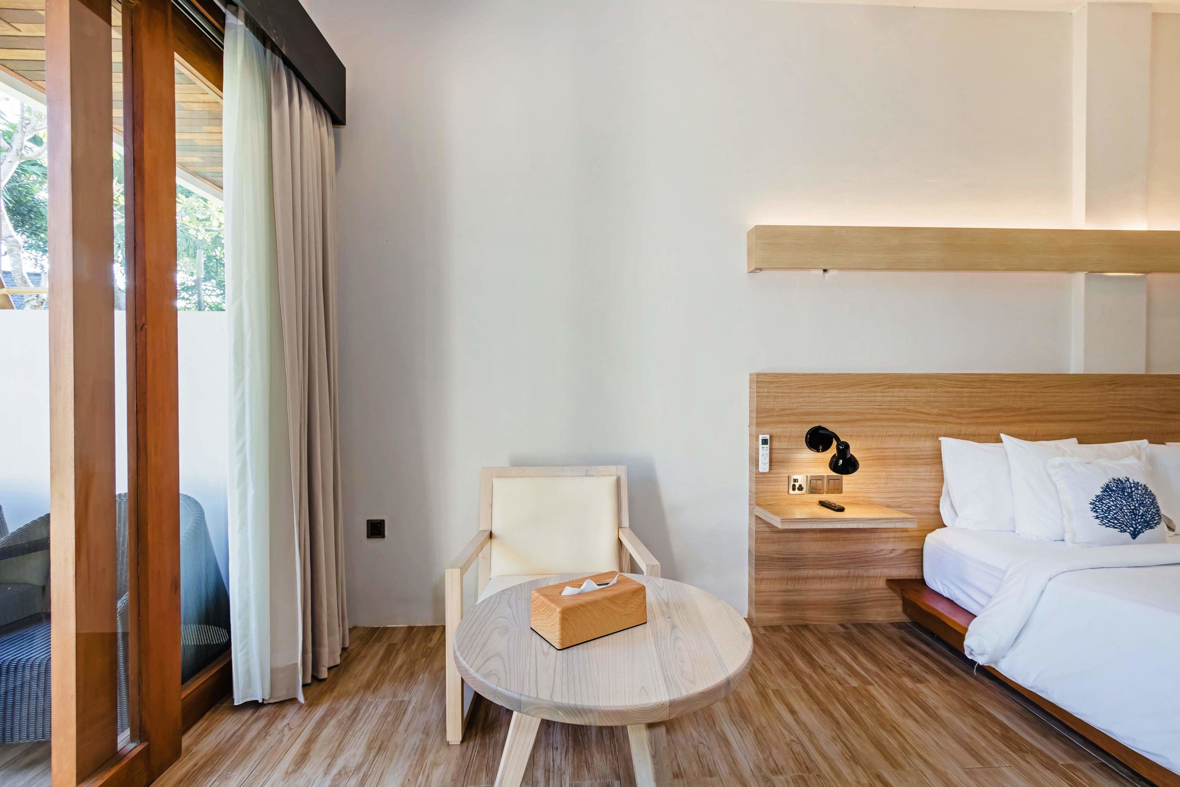 A hotel room with a bed, bedside table, lamp, chair, and round table.
