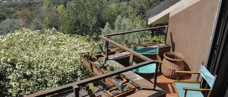 Un balcón con plantas en macetas, una cesta de mimbre y una silla de madera.
