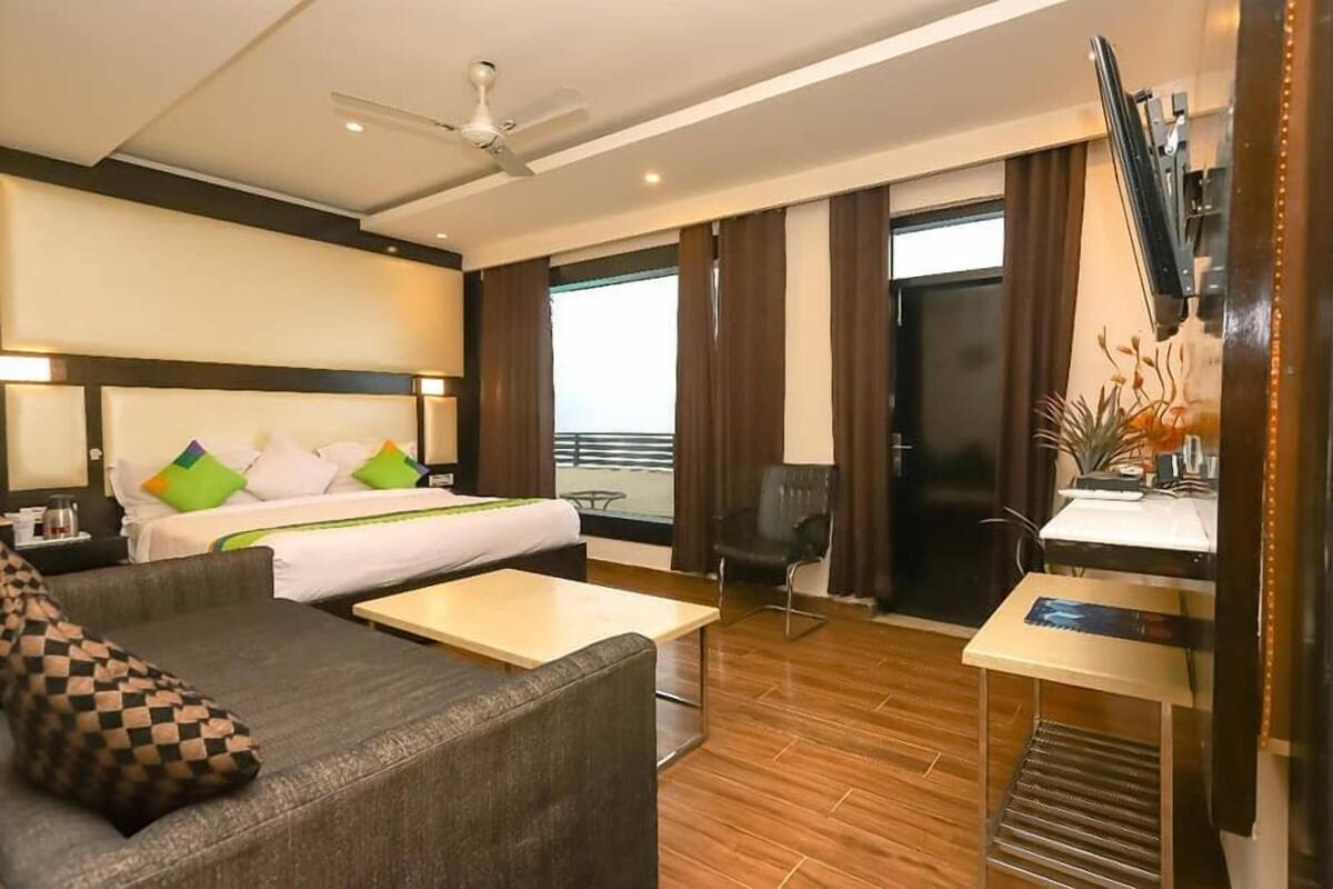 Quarto de hotel com cama, sofá, escrivaninha, cadeira, ventilador de teto e vista para o exterior.