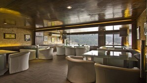 Un restaurant amb taules i cadires altes, una zona de bar i vistes a les muntanyes a través de grans finestres.