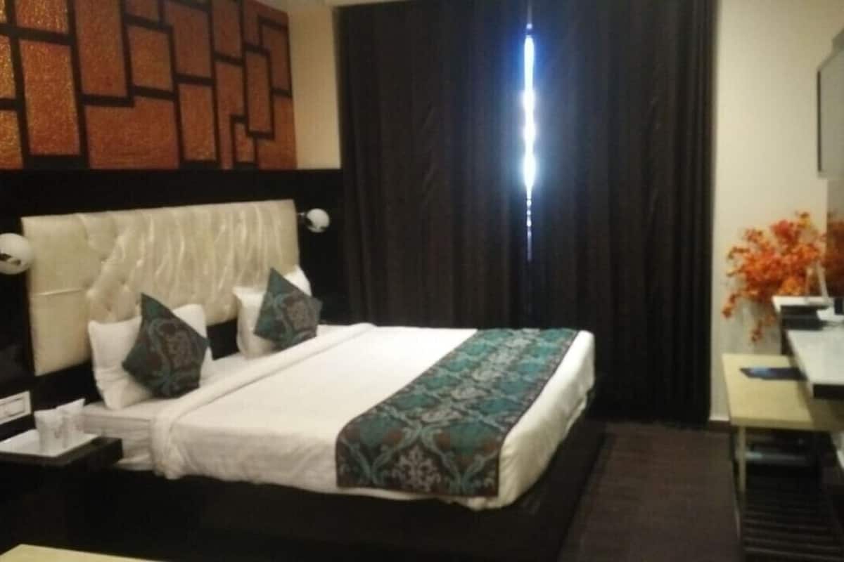 Quarto de hotel com cama, escrivaninha, cadeira, televisão e cortina.