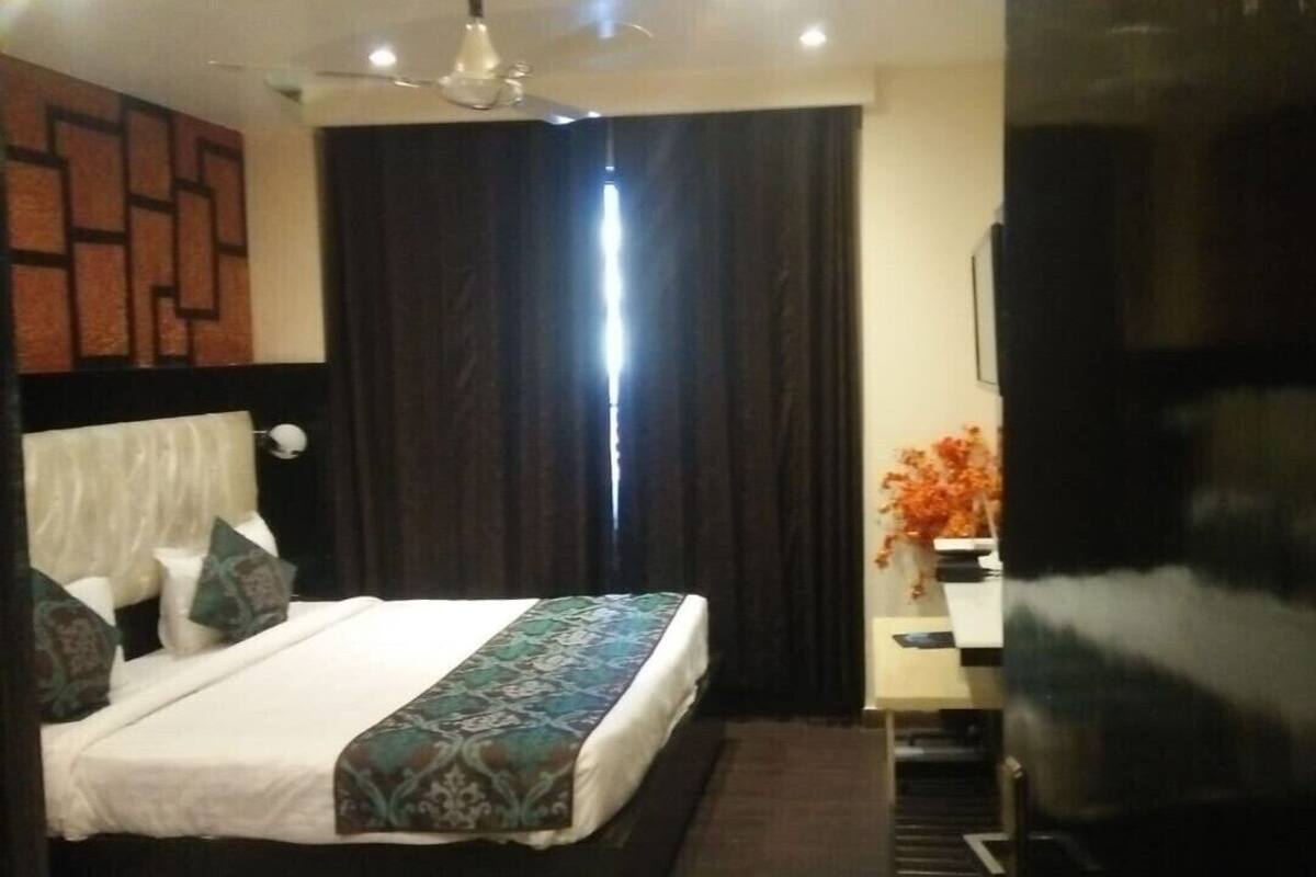 Quarto de hotel com cama, escrivaninha, cadeira, televisão e janela com cortinas.