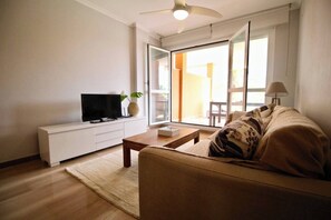 A living room with a sofa, coffee table, TV, and a sliding glass door leading to an outdoor area.