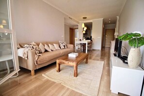 A modern living room with a sofa, coffee table, and a dining area in the background.