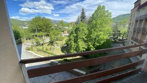 Un balcón con vistas a un patio, árboles y montañas lejanas.