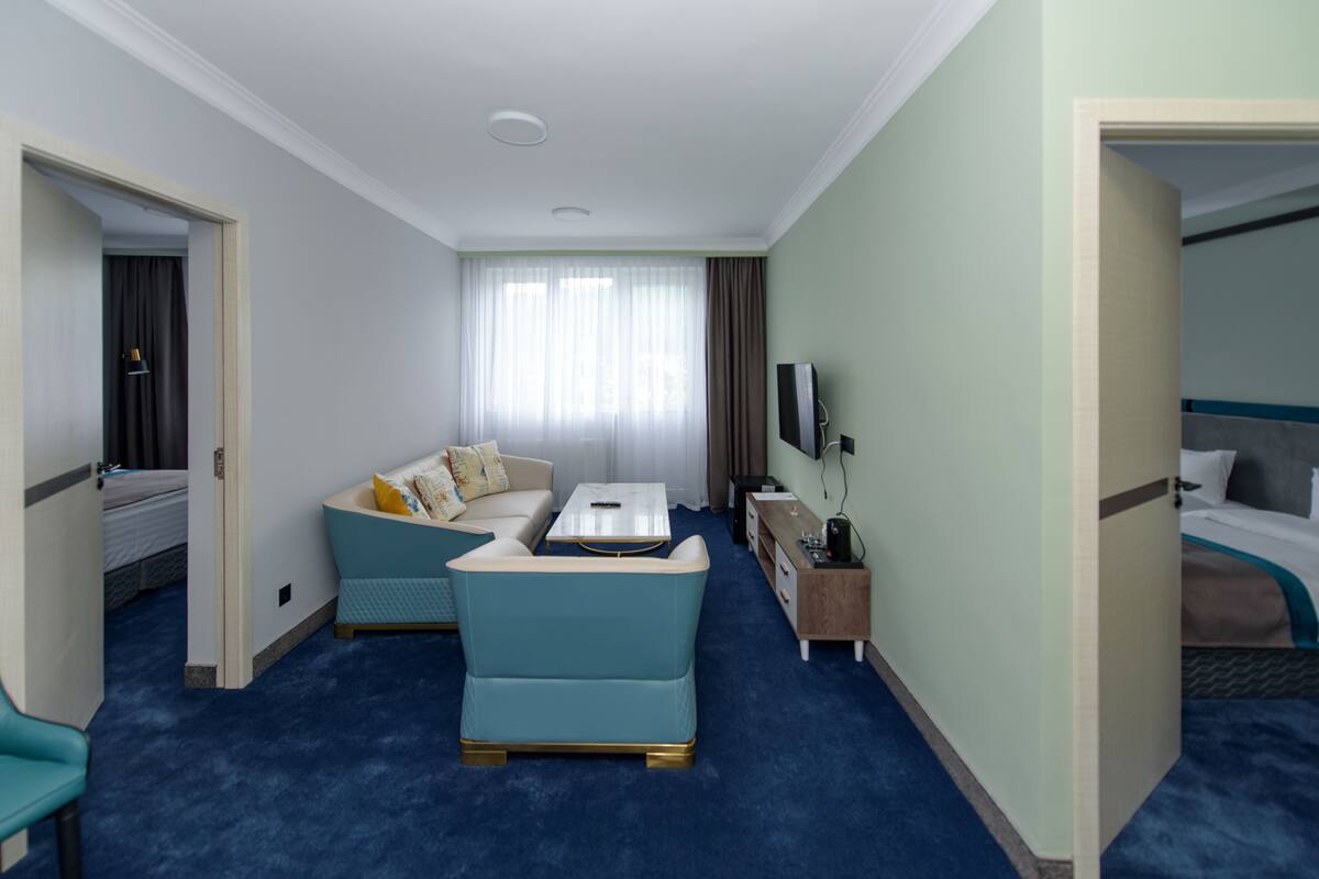 Quarto de hotel com carpete azul, sofá, mesa de centro, televisão e cama.