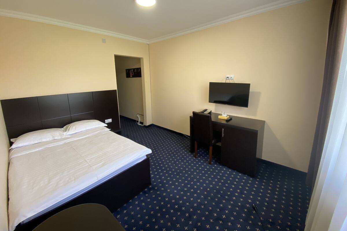 Quarto de hotel com cama, escrivaninha, cadeira, televisão e uma pequena mesa.