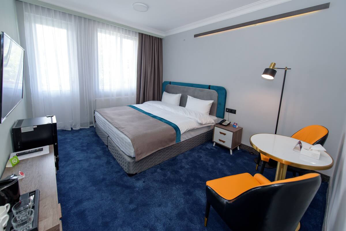 Quarto de hotel com cama, escrivaninha com computador, cadeira, mesa e abajur.