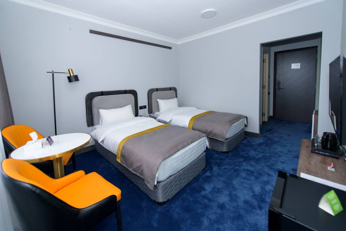 Quarto de hotel com duas camas, uma escrivaninha, uma cadeira e uma televisão.