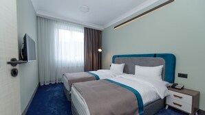 Una habitación de hotel con dos camas, televisión, mesita de noche con teléfono y ventana con cortinas.