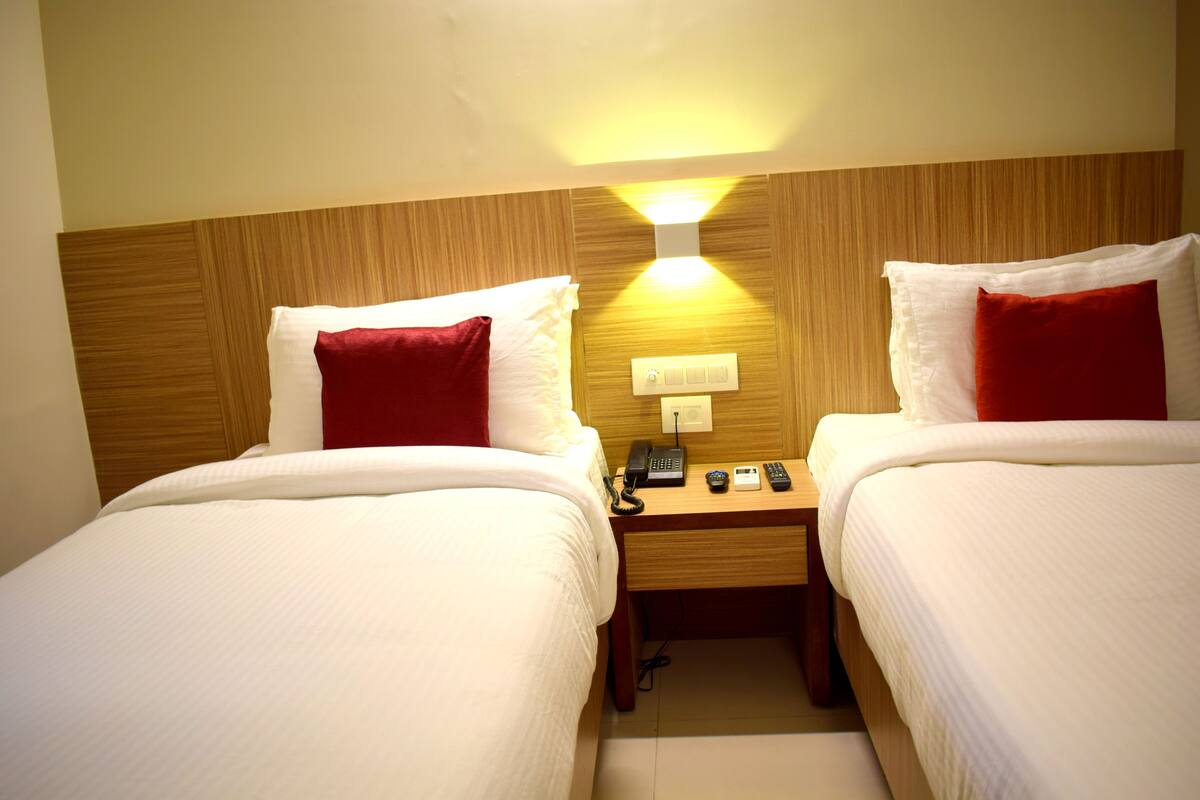 Ein Hotelzimmer mit zwei Betten, jeweils mit weißer Bettwäsche und roten Kissen, einem Holz-Kopfteil, einem Nachttisch mit Telefon und Lampe sowie einer Wandleuchte.