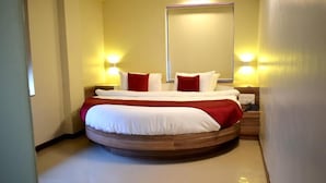 Un lit rond avec un cadre en bois, une literie blanche et des touches de couleur rouge. Il y a deux lampes de chevet et un miroir au-dessus du lit.