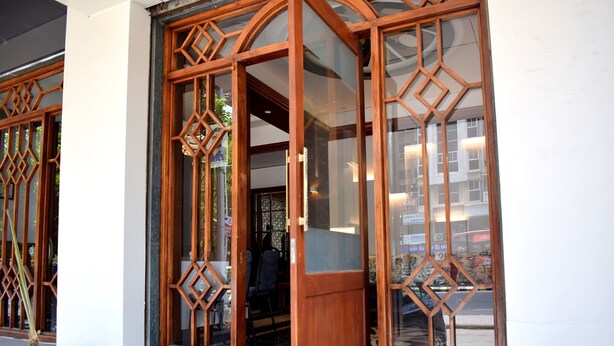 Une entrée d’immeuble avec une porte en bois et des panneaux de verre, ornée de motifs géométriques.