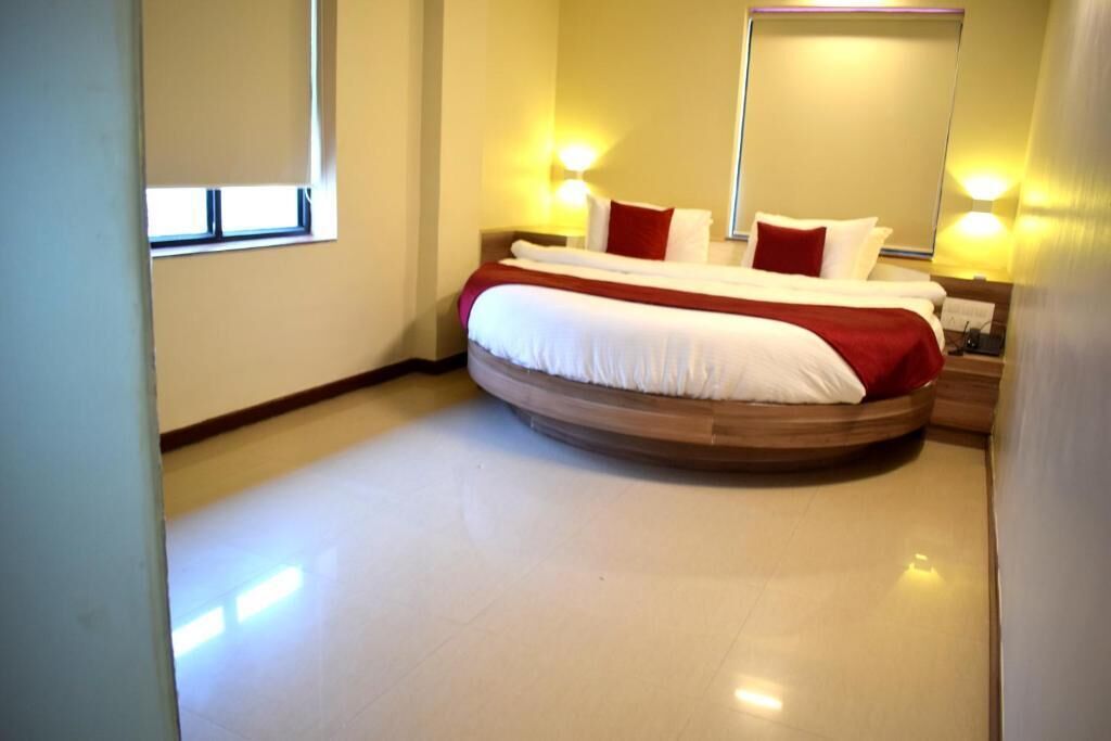 A hotel room with a large bed, two bedside lamps, a window, and a mirror.