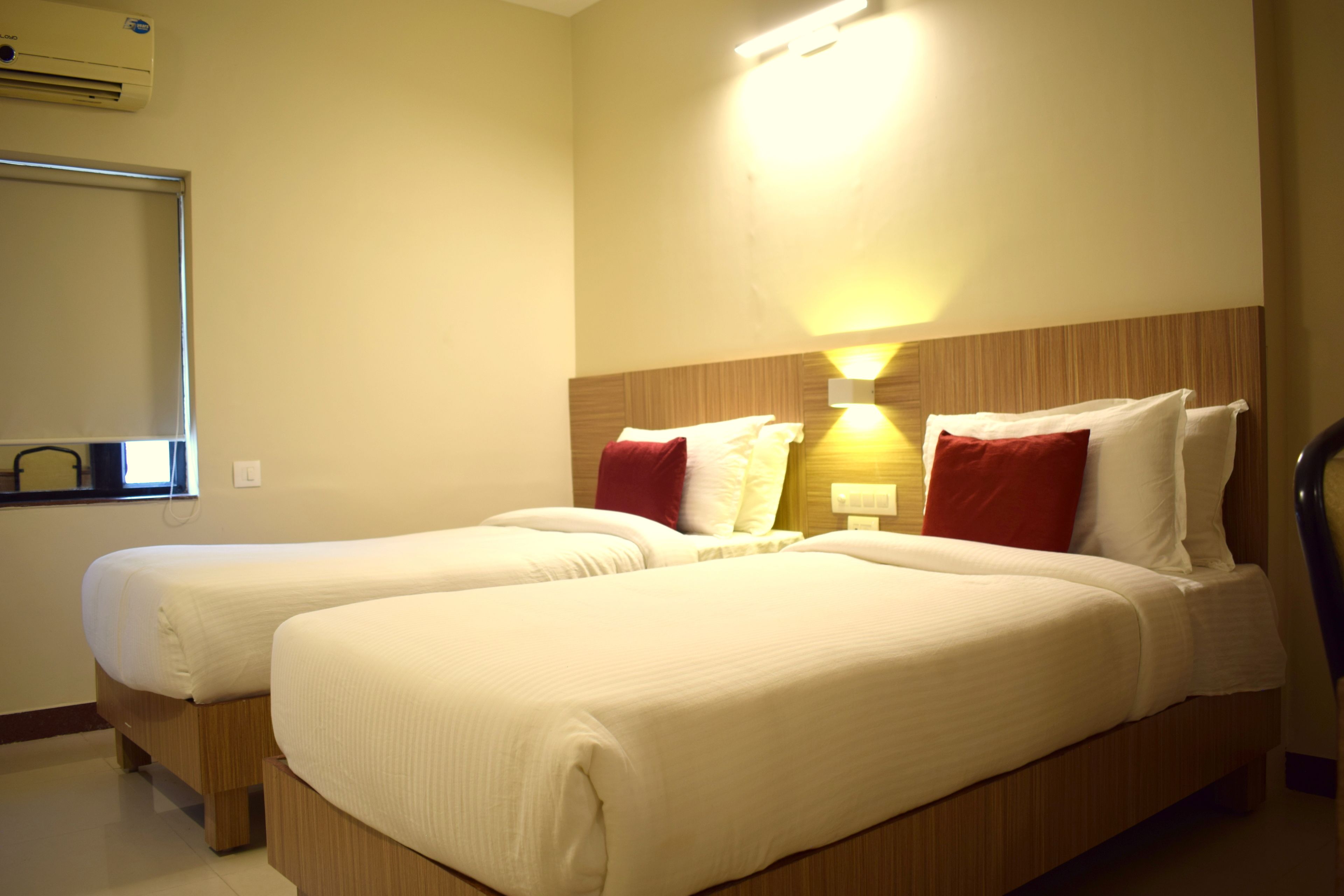 Habitación de hotel con dos camas, cabecero de madera, aire acondicionado de pared y ventana con persianas.