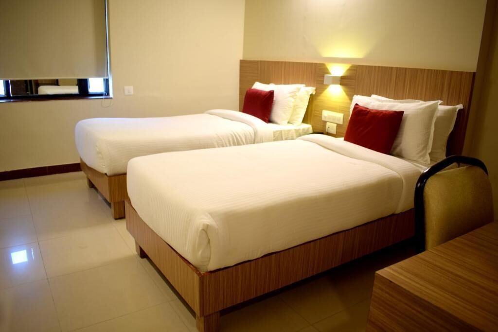 Ein Hotelzimmer mit zwei Einzelbetten, einem Holzkopfteil, einem Nachttisch und einer Wandleuchte.