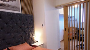A bedroom with a tufted headboard, a bed with an orange quilt, a bedside table with a lamp, and a wooden partition. - Apartment Rustica Zadar with exclusive use of pool & yard (Zadar)